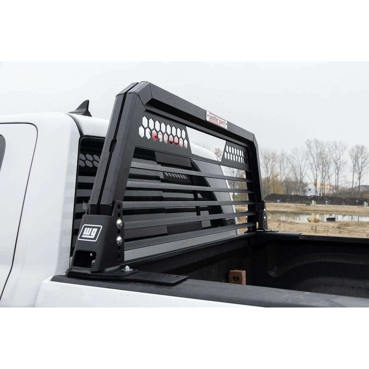 A black metal headache rack with horizontal bars and hexagonal cutouts is mounted on the bed of a white Ford pick-up truck. A black metal headache rack with horizontal bars and hexagonal cutouts is mounted on the bed of a white Ford pick-up truck.