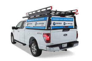 A white Ford Vocational Pick-up with a canopy featuring blue Driverge and U.S. Upfitters branding and a black roof rack, viewed from the rear passenger side. A white Ford Vocational Pick-up with a canopy featuring blue Driverge and U.S. Upfitters branding and a black roof rack, viewed from the rear passenger side.