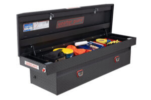 A black Weather Guard truck toolbox is open in the bed of a Ford pick-up truck, revealing various tools and supplies including a tape measure, gloves, a roller brush, safety vest, and containers. A black Weather Guard truck toolbox is open in the bed of a Ford pick-up truck, revealing various tools and supplies including a tape measure, gloves, a roller brush, safety vest, and containers.