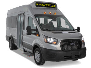 A silver Ford Minibus passenger shuttle van with a front entry door and an overhead digital sign reading DRIVERGE VEHICLE IN.