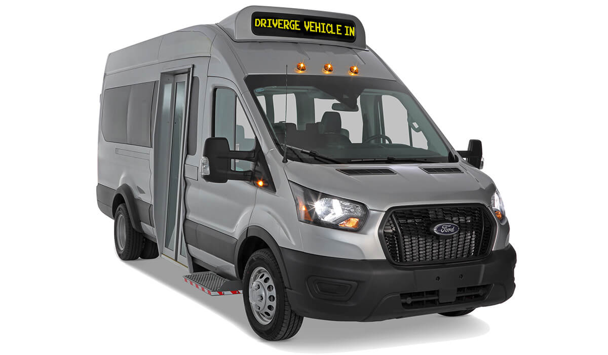 A silver Ford Minibus passenger shuttle van with a front entry door and an overhead digital sign reading DRIVERGE VEHICLE IN.