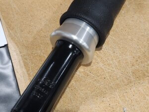 A black and silver motorcycle handlebar grip with a throttle tube, resting on a wooden surface near a cardboard box.