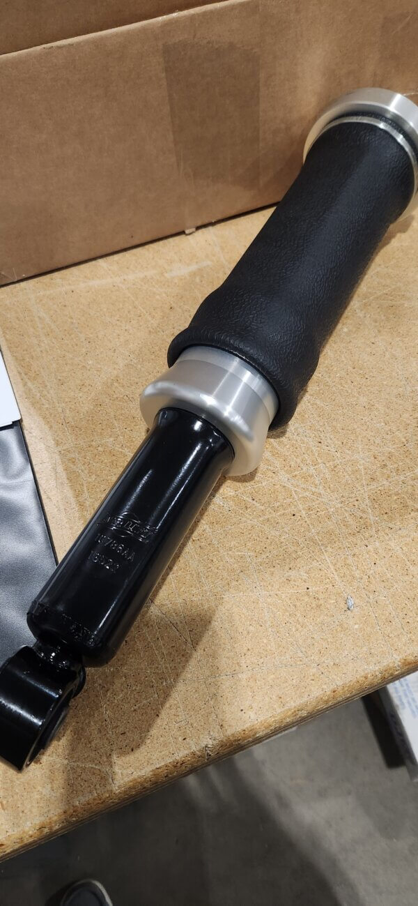 A black and silver motorcycle handlebar grip with a throttle tube, resting on a wooden surface near a cardboard box.