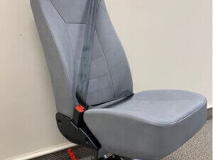 A single gray car seat with a seatbelt attached, mounted on a metal base, positioned against a plain wall on a carpeted floor.