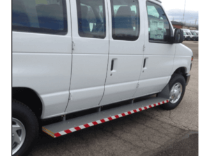 A white passenger van with a red and white striped side step parked on an asphalt surface.