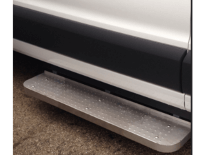 A close-up of a metal running board attached to the side of a white vehicle, positioned above an asphalt surface.