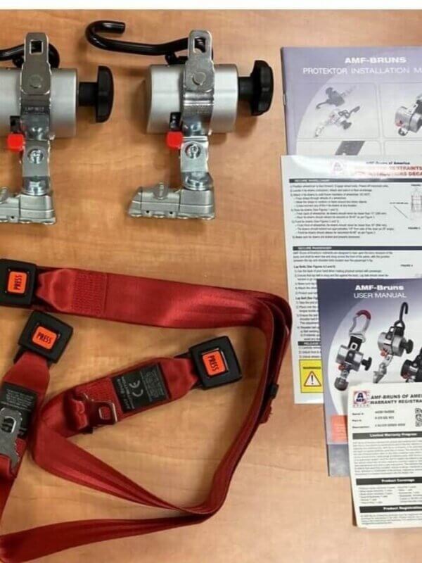 Two metal retractors, red seat belts with buckles, and several instruction manuals and safety leaflets are laid out on a wooden surface.