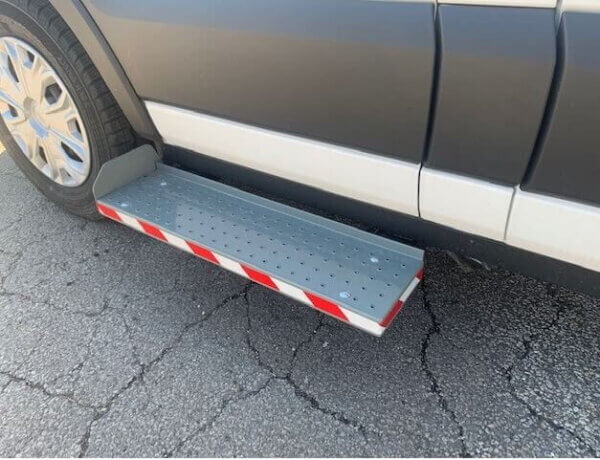 A metal running board with red and white reflectors is mounted below the door of a parked vehicle on a cracked asphalt surface.