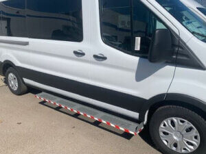 A white passenger van with a side door and a metal running board featuring red and white diagonal stripes.