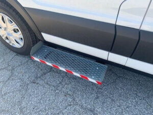 A metal side step with a diamond plate pattern and red and white reflective tape attached below the door of a white vehicle.