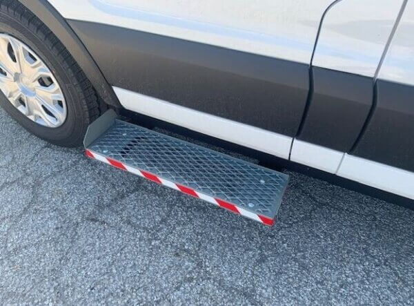 A metal side step with a diamond plate pattern and red and white reflective tape attached below the door of a white vehicle.