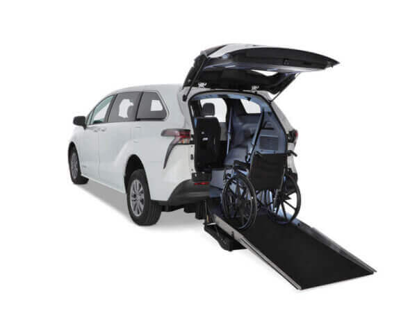 A white Toyota Sienna Hybrid minivan with its rear hatch open, showing a wheelchair on a rear-entry ramp leading into the vehicle’s interior.