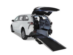 A white Toyota Sienna Hybrid minivan with its rear hatch open reveals a lowered ramp for convenient rear-entry wheelchair access.