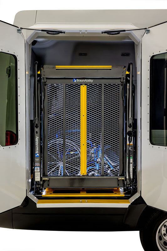 A rear view of a van with open doors, showing a BraunAbility wheelchair lift in the lowered position, ready for use.