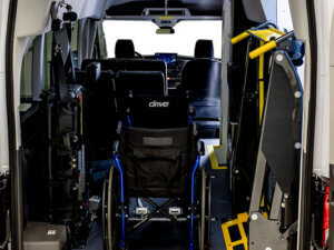 The rear view of a van shows a wheelchair secured inside, ramp equipment, and seats arranged for accessible transportation.