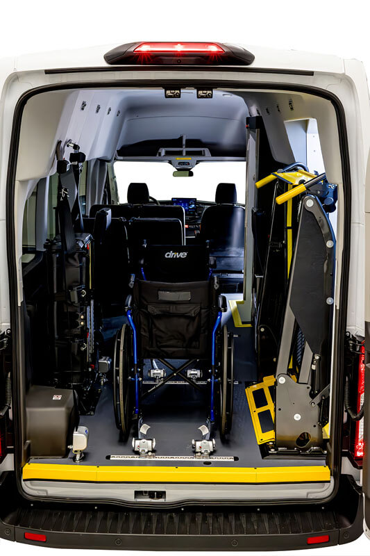 The rear view of a van shows a wheelchair secured inside, ramp equipment, and seats arranged for accessible transportation.
