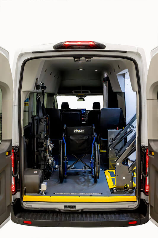 The interior of a wheelchair-accessible van is shown from the back, with a secured wheelchair, ramp, and seating visible.