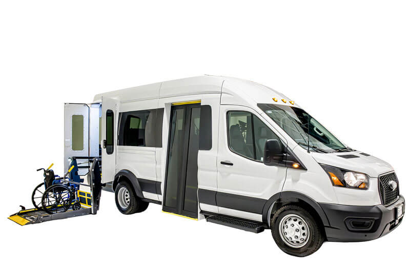 A white passenger van with a side door open and a wheelchair lift extended, loading a blue wheelchair into the vehicle.